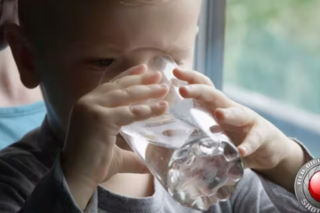 Little Boy Drinking Water From A Glass And Smiling With Mom Holding Him By The Window by revleha on